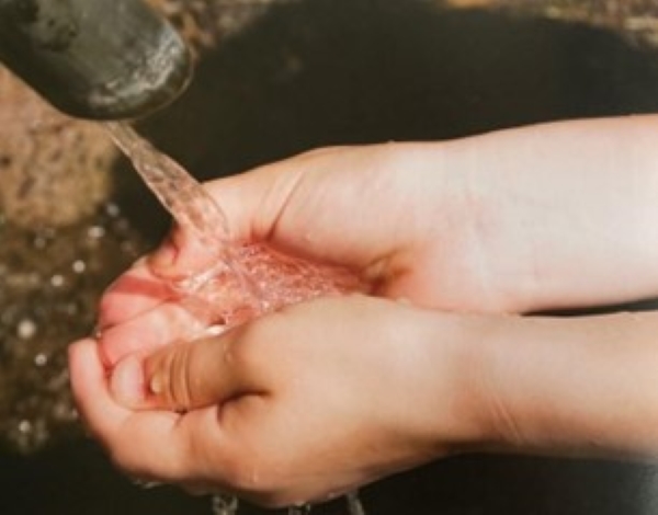 Hands capturing clear running water from a spout.